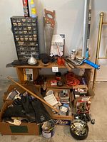 Overview of wooden shelf with various garage tools including saw, oil cans, extension cord, brushes, funnel, gloves, and boxes of small parts