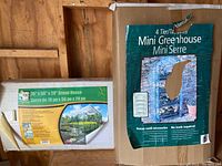 Photo shows boxes of two greenhouses: a mini 4-tier tabletop greenhouse and a 76" x 56" x 28" outdoor portable greenhouse with detailed specs on the box.