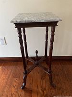 Full view of the marble top plant stand with wooden ornate base on hardwood floor.