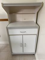 Front view of white microwave stand showing drawer and cabinet doors with silver handles.
