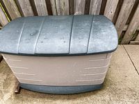 Closed Rubbermaid outdoor storage container showing weathered lid and sides against a wooden fence.