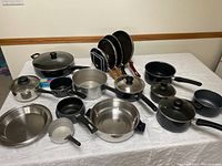 Wide view of assortment of pots and pans on a white surface showing various types and sizes