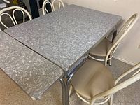 Top and side view of retro table with extendable leaves opened at both ends, showing marbled laminate surface and four matching chairs around it.