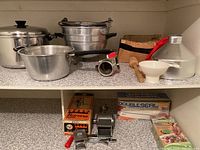 Overview of large pots, strainers, bowls, wooden masher, metal funnel, and double sealer machine parts on countertop