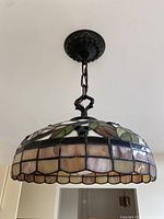 Photo showing stained glass dome light fixture hanging from ceiling with a dark metal chain, displaying floral and leaf design on shade.