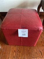 Red vinyl cube-shaped stool with stitched cross pattern on top, placed on wood floor.