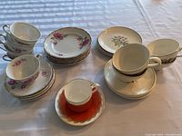 Photo showing the collection of six teacups, saucers stacked, and serving plates, all with floral pink rose patterns and gold trim on a table.