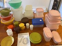 Full lot of assorted vintage Tupperware containers, cups, bowls, and original publication laid out on a wooden table.