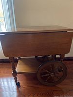 Full side view of vintage wooden bar cart with drop-leaf sides folded down and wagon wheel side wheels.