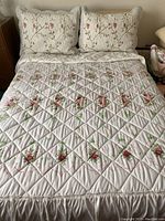 Full view of bed with quilt and two shams featuring floral patterns and diamond quilting on white fabric