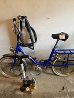 Side profile of blue vintage Graziella folding bicycle with floor pump, lubricant spray, and two small maintenance containers placed at the front wheel, showing the full bike frame, saddle, and some wear.