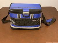 View of front of cooler bag showing blue top, black and blue sides, AirLok branding on front pocket, and adjustable black shoulder strap.