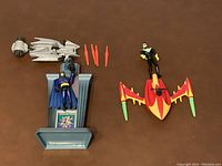 Batman figure on crime bust pedestal with Batmobile, launcher, missiles, Nightwing figure and attack craft arranged on a brown surface