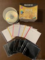 Box of 20 sealed Sony DVD-R discs, spindle of blank CDs, 6 loose DVDs with labeled writable cases.