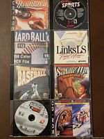 Top view of eight PC CD-ROM sports game cases arranged in two vertical columns, titles visible include Hardball III, Galaxy of Sports, Hardball 6, Links LS Trial Nine, General Admission Baseball, Saddle Up Time to Ride, MLB 2K9, Summer and Winter Olympic Challenge.