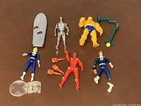 Top-down image showing all six Fantastic Four action figures and accessories spread out on a brown surface, revealing condition and completeness.