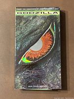 Front cover of Godzilla (1998) VHS showing close-up of Godzilla's eye with text and graphics.