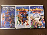 Front covers of three VHS tapes: Justice League, Challenge of the Super Friends: Attack of the Legion of Doom, and Super Friends: United They Stand Volume 2