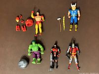 Full overview photo of all five Marvel action figures with accessories scattered around them on a brown surface.