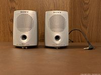Front view of Sony SRS-P7 left and right stereo speakers with speaker grills, front port, and attached audio cable.