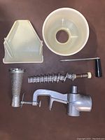 Disassembled parts of the tomato press showing metal press, filter, screw, and plastic hopper and collector.