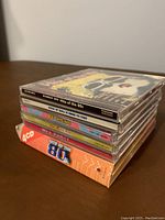 Side view of six stacked CD cases with visible spines showing titles referencing 80's music hits.