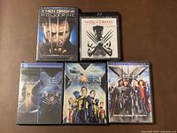 Overview photo showing all seven DVD cases of X-Men movies arranged in two rows on a brown surface.