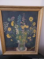 Front view of the framed painting showing a colorful wildflower bouquet in a glass vase against a dark backdrop.