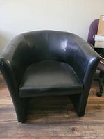 Front view of one black faux leather club chair with curved arms and cushioned seat