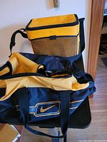Yellow cooler bag with mesh front pocket and black zipper placed behind the Nike duffle bag on a table.