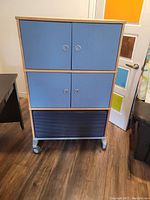 Front view of the blue and black mobile dresser storage cabinet showing two sets of blue double doors and one black drawer at bottom on wheels.