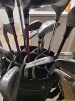 Photo of golf clubs in the golf bag showing various iron clubs, drivers, woods, and a putter, with visible numbering on club heads.