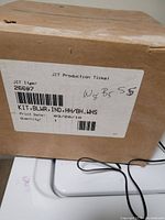 Brown cardboard box with JIT production ticket label showing item number 26607 and description KIT.BLWR.IND.HH/BH.WHS dated 03/20/19. Box is sealed with visible attached wires.