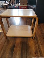 Full view of small wooden side table with lower shelf and one side wheels.