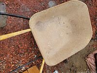 Top down view of the weathered metal tray of the wheelbarrow on the ground with mulch.