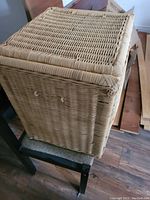 Wicker rectangular laundry hamper showing the missing handle on one side and intact handle on the other side.