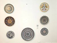 Seven artisan ceramic wall plates arranged on white wall showing varied Mediterranean and Deruta style hand painted designs.
