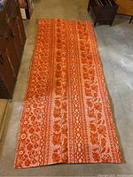 Full view of the orange and white floral patterned rug laid flat on floor.