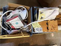 Boxes containing craft show display items, including white flexible-neck lamps, a clip-on light, wooden stands, and miscellaneous items.