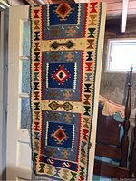 Floor runner hanging on door showing geometric and floral designs in blue, cream, red, green, brown, black, and beige colors.