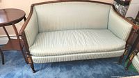 Front view of light blue damask upholstered loveseat showing wooden frame and cushion