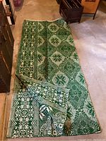 Full view of green and white runner rug with floral and geometric design folded on a concrete floor.