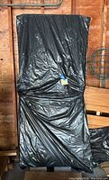 Two folded tables wrapped in black plastic sheeting leaning against wooden wall