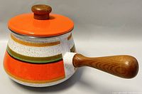 Side view of the vintage 1970s enamel fondue pot showing colorful enamel finish and wooden handle.