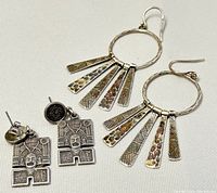 Photo shows two pairs of earrings: one pair of circular hoops with five patterned drop rectangles each, and one pair with square face design and black stone studs.