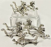 Eight miniature pewter dragon figurines displayed on a white surface with one raised on a clear stand to show details.