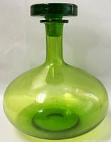 Side view of a green glass bottle with rounded body and tapered neck, topped with a flat circular stopper.
