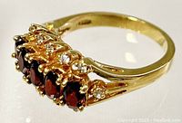 Close-up view of the ring's top showing five oval red stones and clear crystals on a gold-colored setting.