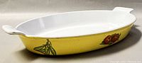 Photo of oval casserole dish showing one end with painted peas on yellow enamel exterior and white enameled interior.