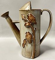 Front side showing raised bird and branch embossed design on the watering can shaped vase with beige and brown glaze.